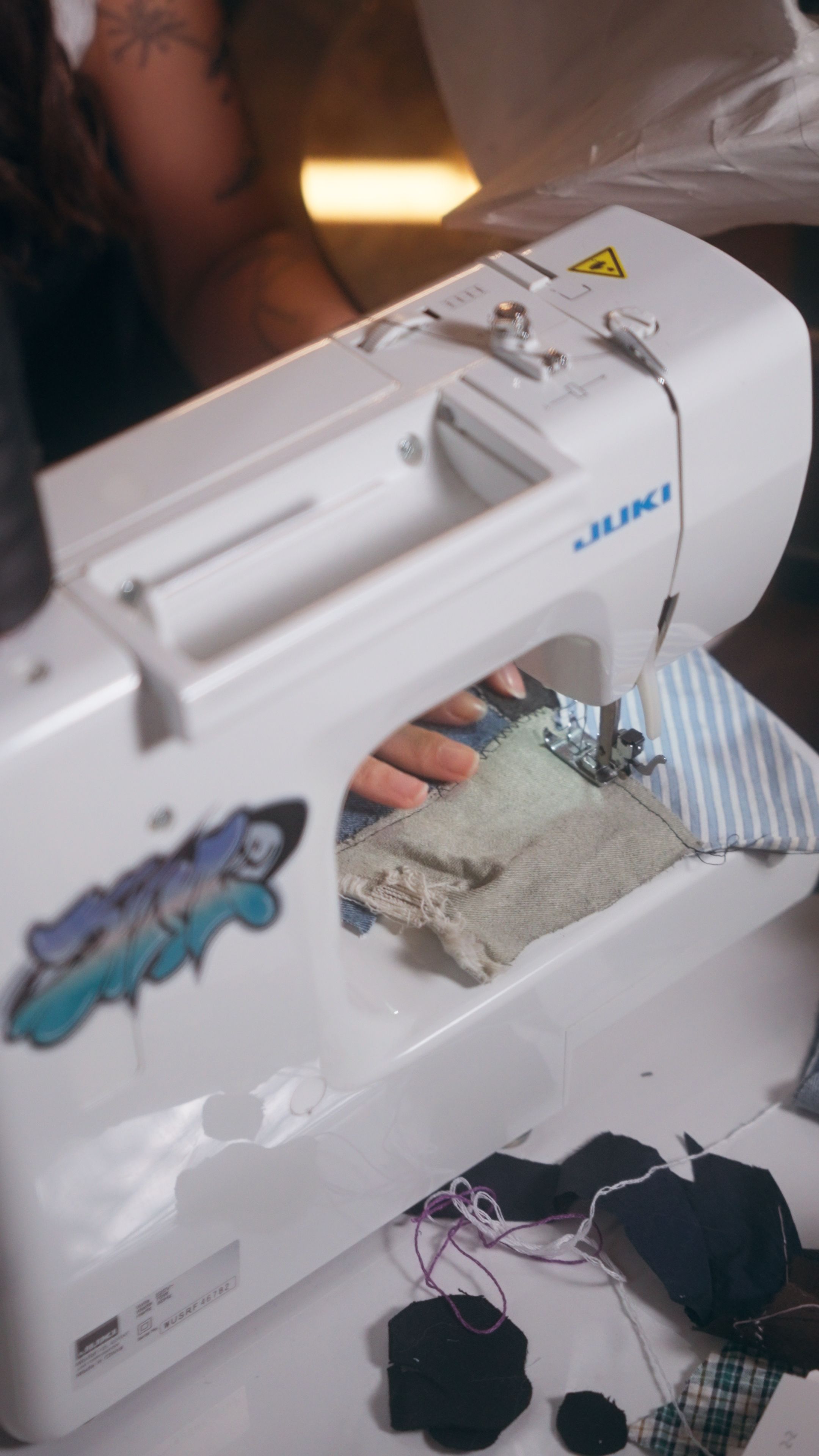 A sewing machine stitches recycled fabrics, highlighting Nicole Ng’s handcrafted textile art creation process.