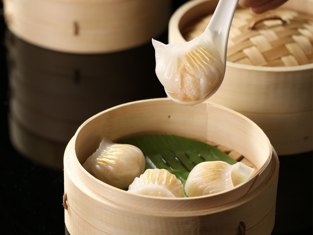 美狮美高梅”淳“的淳鲜虾饺王摆放在竹蒸笼中，一颗以汤匙提起，展现晶透外皮与饱满内馅